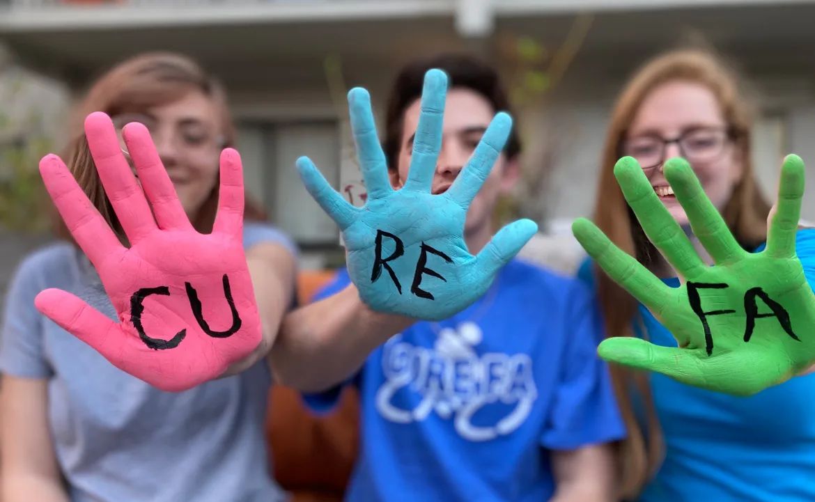 Three women with CURE FA written on hands